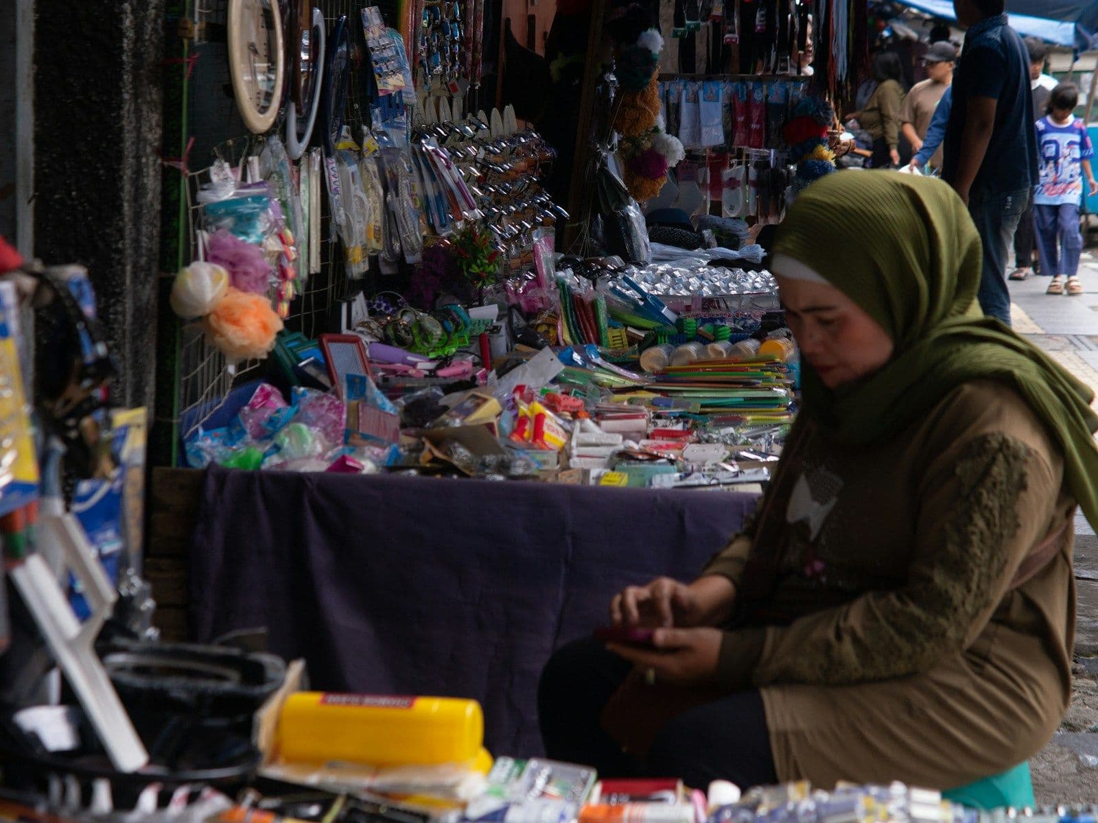 Pedagang perempuan berjilbab duduk di lapak pasar yang penuh barang dagangan