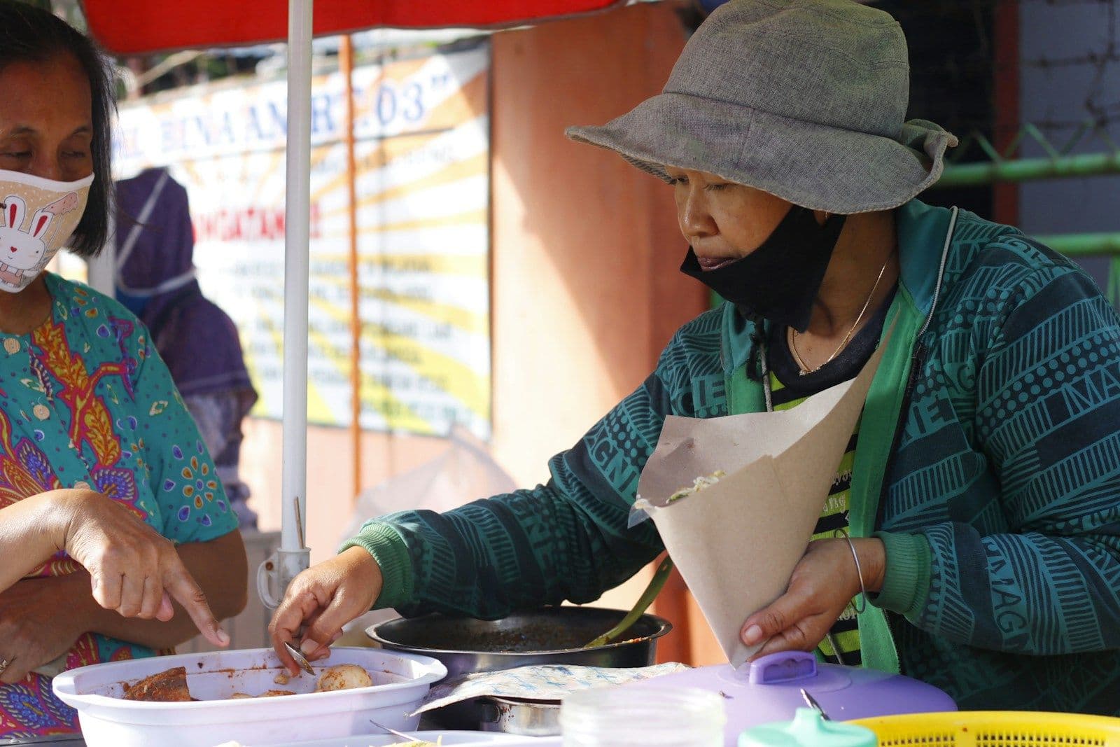 Penjual makanan berapron hijau menyiapkan pesanan di lapaknya